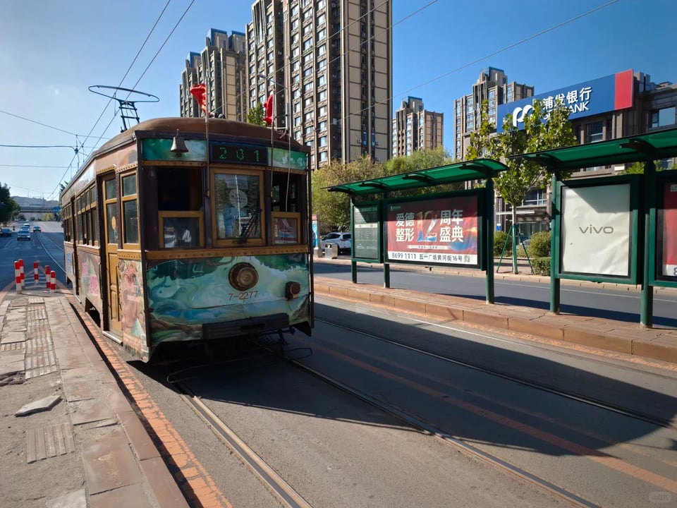 A vintage green tram approaching a street-side stop in Dalian.