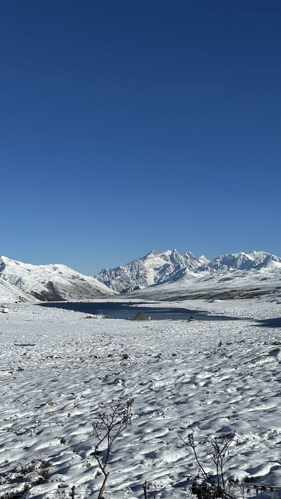 A snow-covered meadow and a small lake beneath snowy peaks.