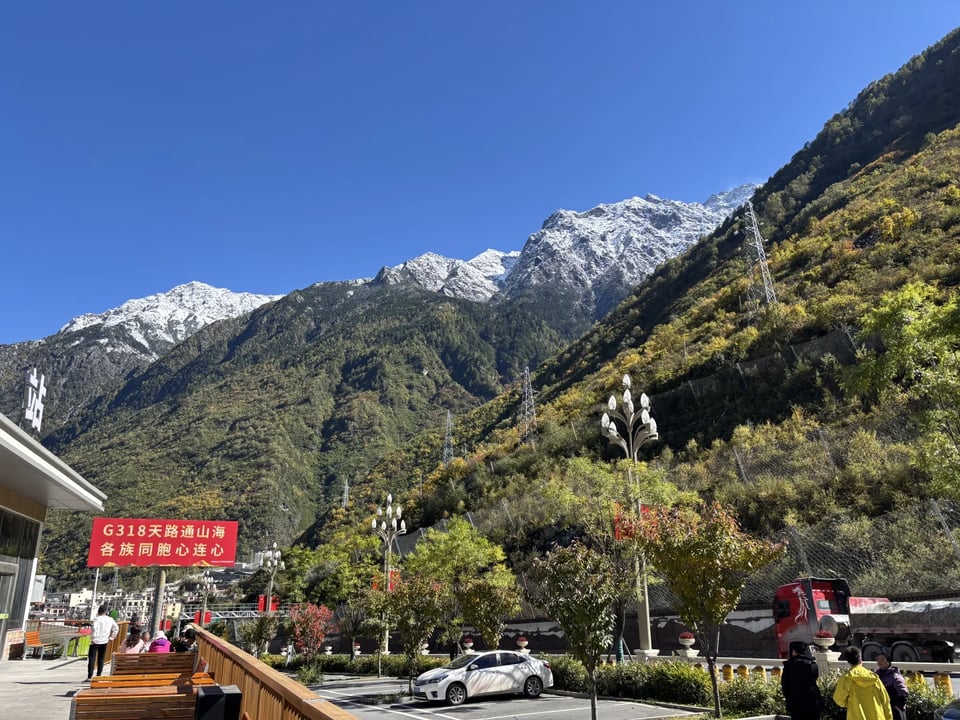Snowy peaks above autumn forest at a G318 rest stop.