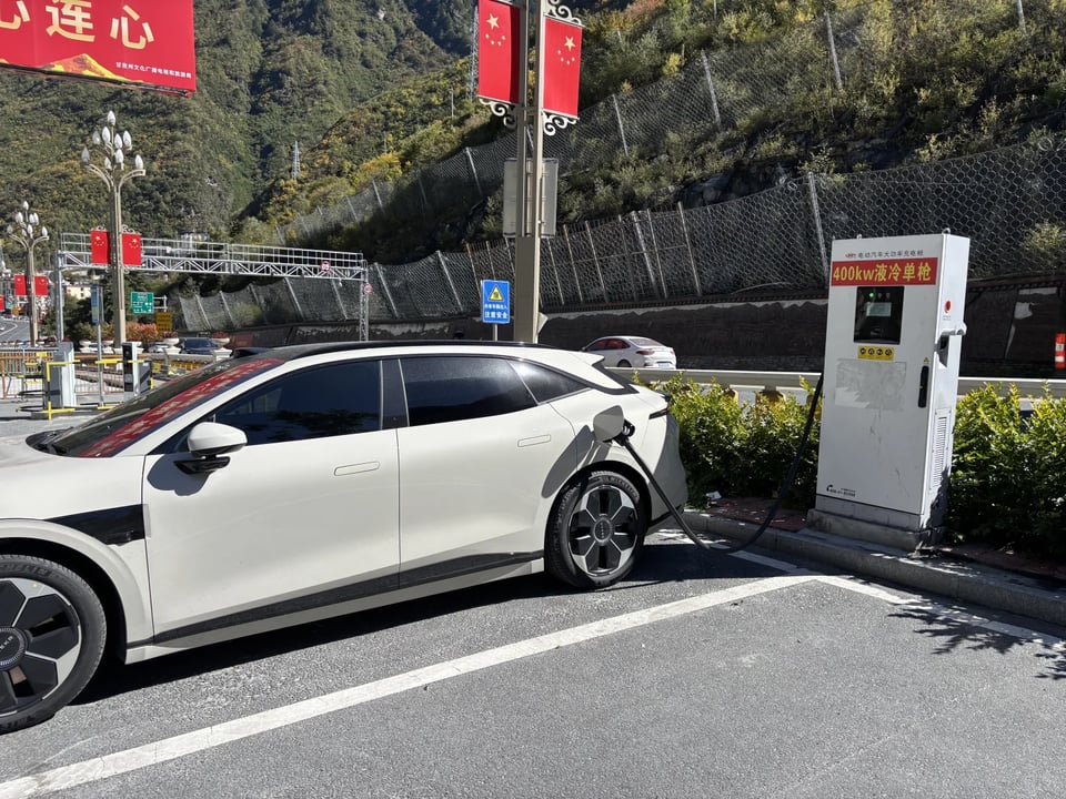 A white car charging at a fast charger beside a mountain road.