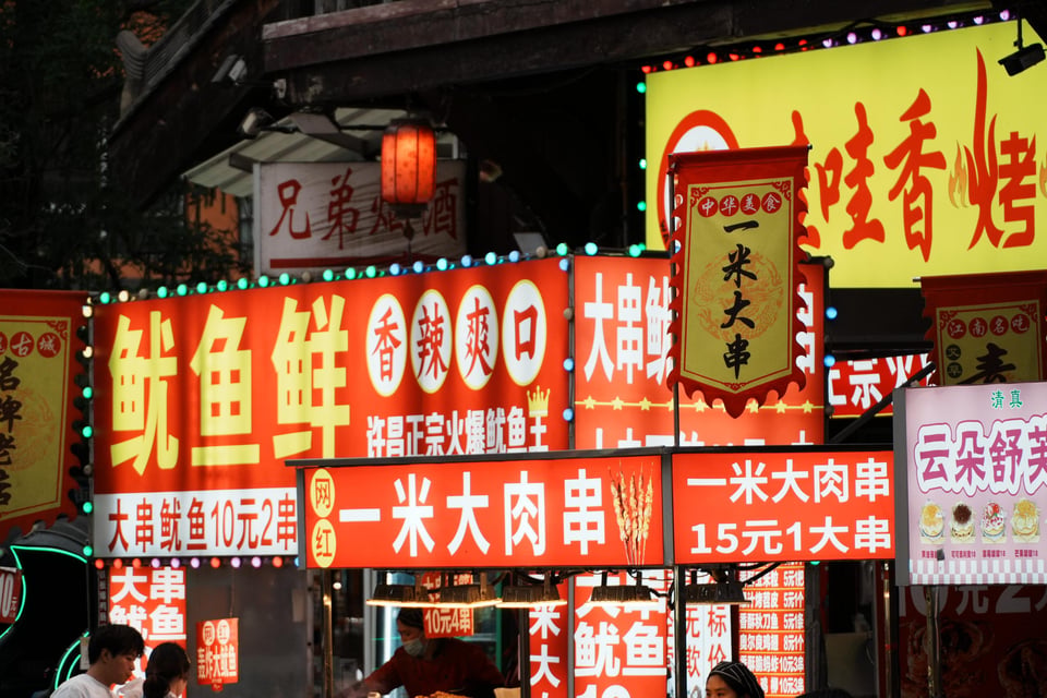 Neon food stall signs advertising squid and meter-long skewers.