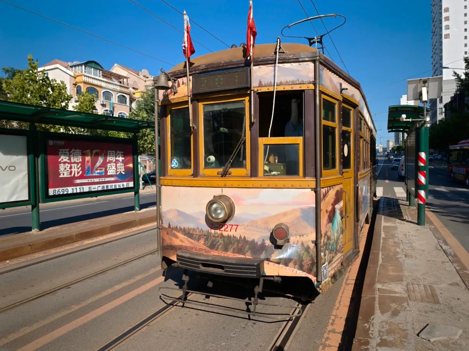 A vintage yellow tram beside a green-roofed tram stop.