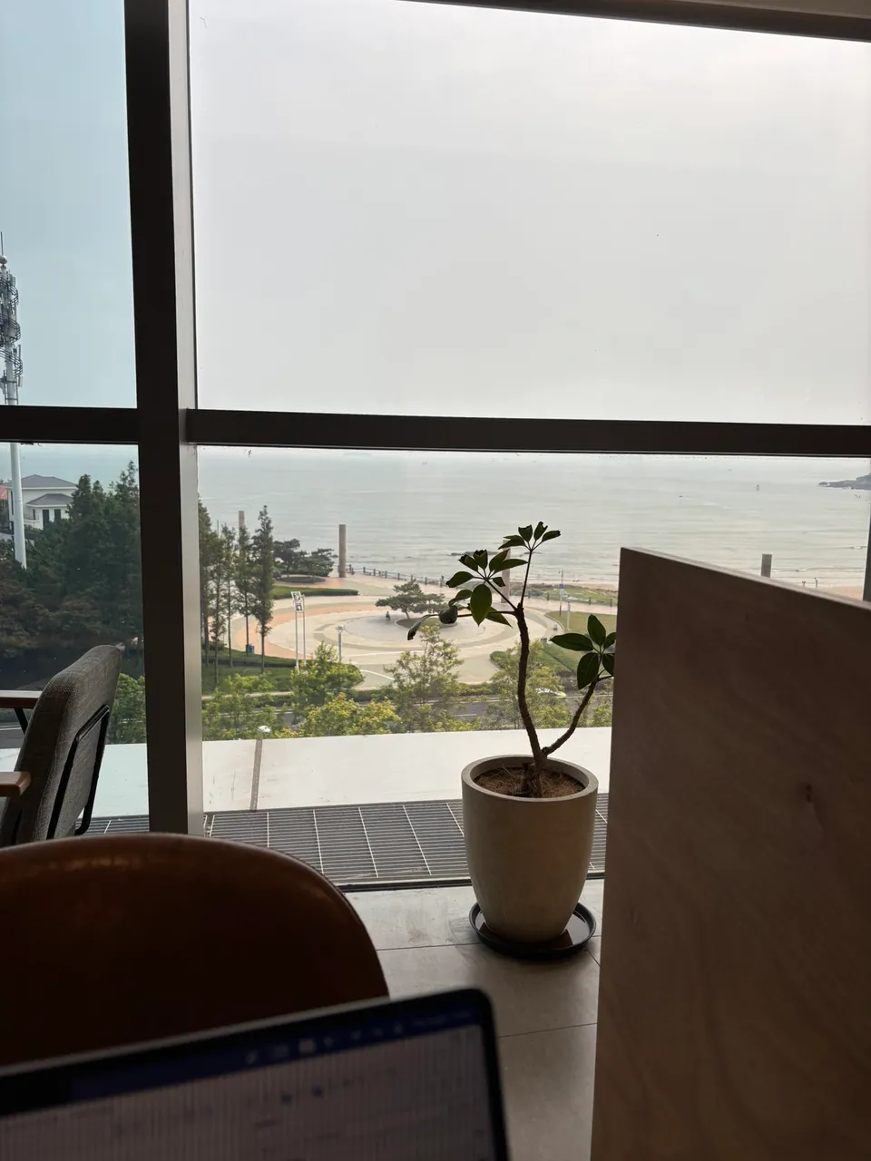 A laptop on a bookstore desk beside a window overlooking the sea and a round seaside plaza.