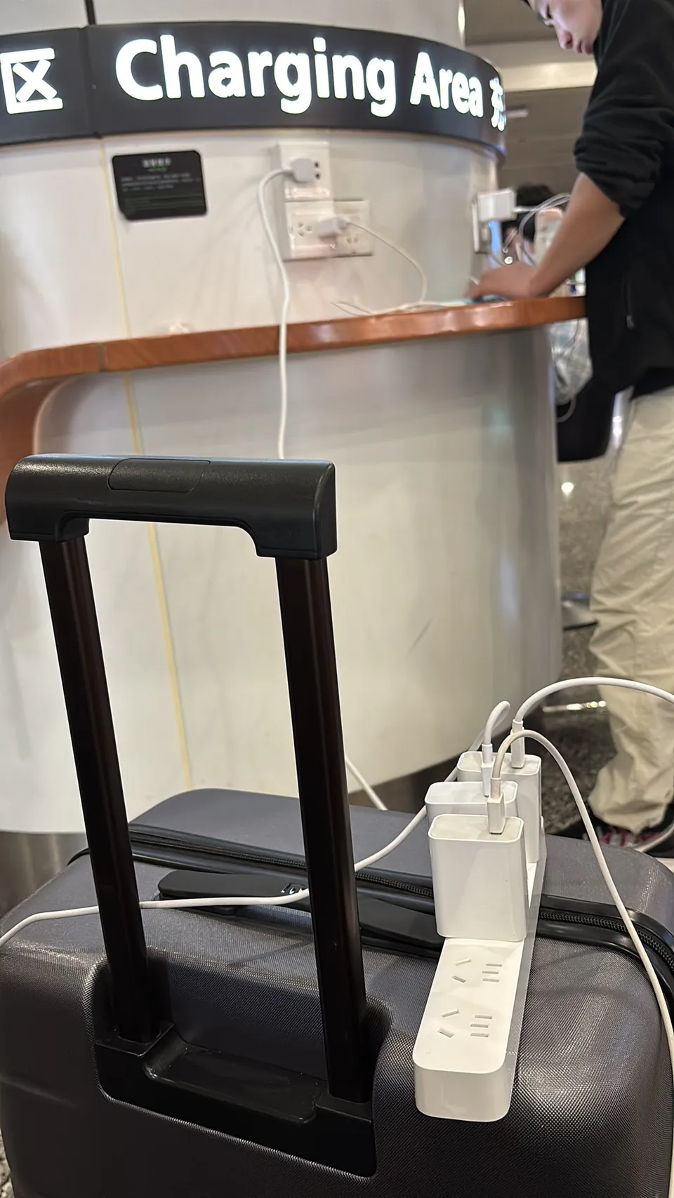 A power strip on a suitcase charging several devices at an airport charging area.