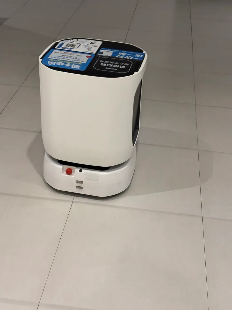 A white delivery robot waiting on a tiled apartment floor.