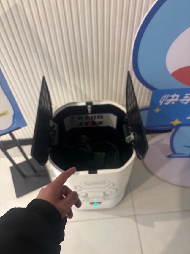 A hand pointing into the open compartment of a delivery robot.