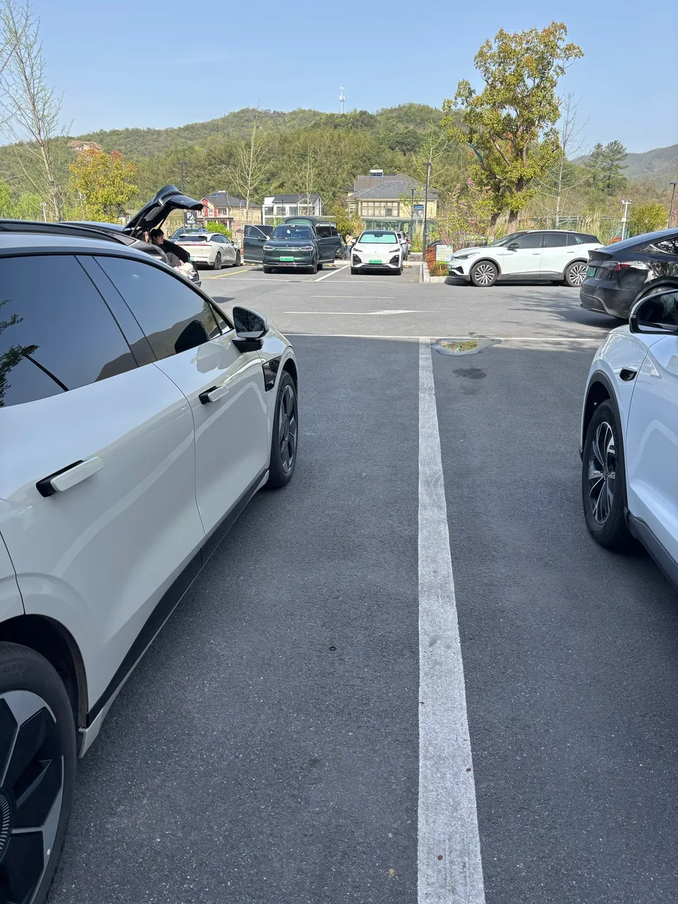 A white car parked in the visitor center lot with green hills behind.