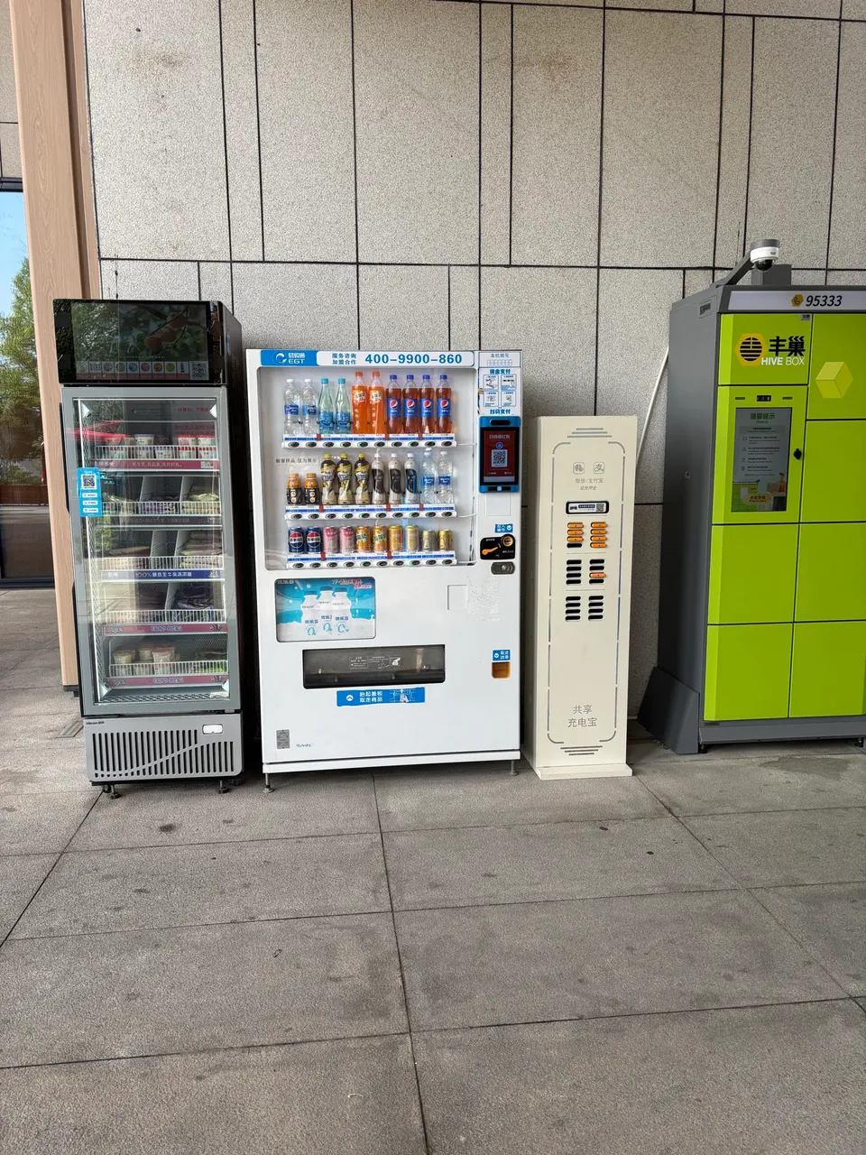 A fridge, drinks vending machine, power bank kiosk, and parcel lockers along a wall.
