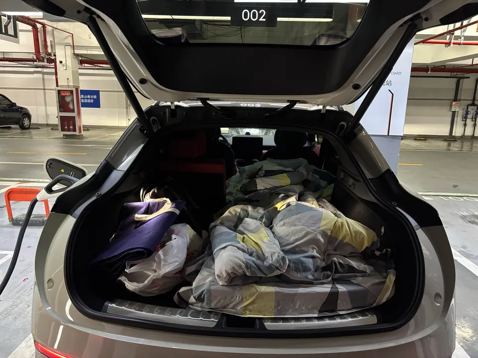 An open car hatch with bedding packed in the trunk at a charging spot.