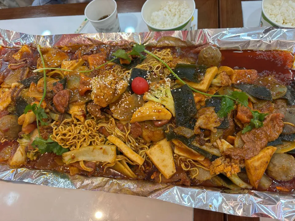 A teppanyaki pan of noodles, vegetables, and meatballs on foil.