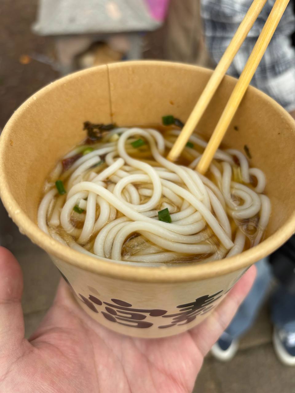 A paper cup of plain rice noodles held in hand.