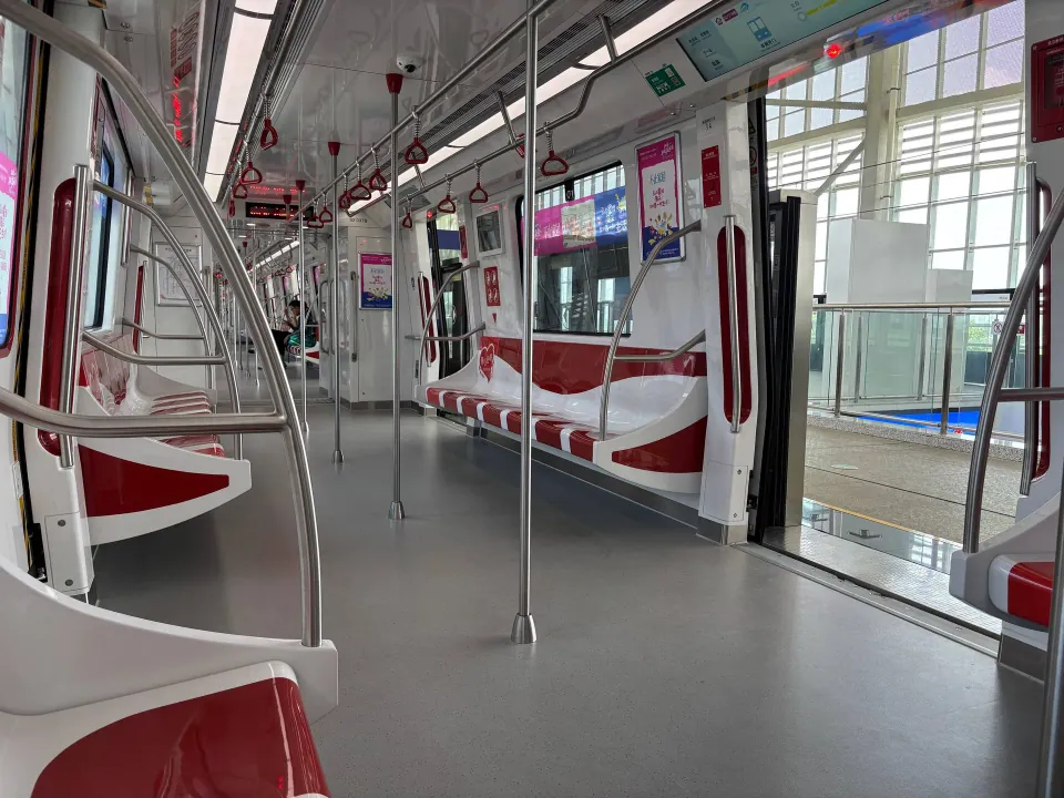 An empty metro carriage with red seats and stainless steel handrails.