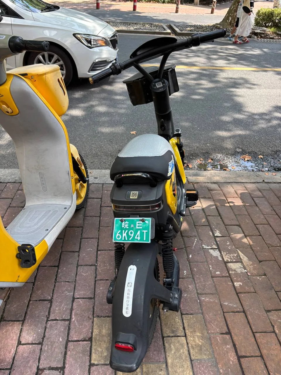 A yellow shared electric scooter parked on a shaded sidewalk.
