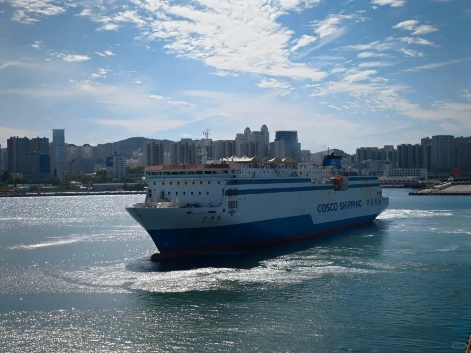 A blue-and-white ferry turning in the harbor beside the city skyline.