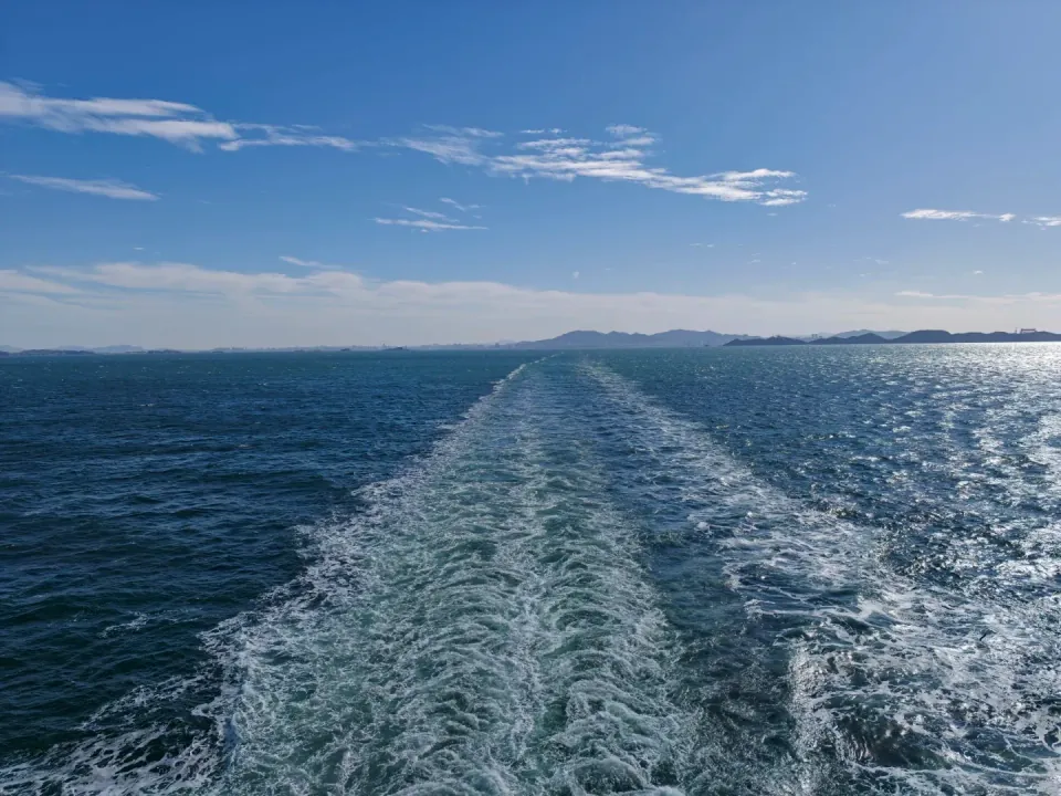 A long white wake trailing behind the ferry across the blue sea.
