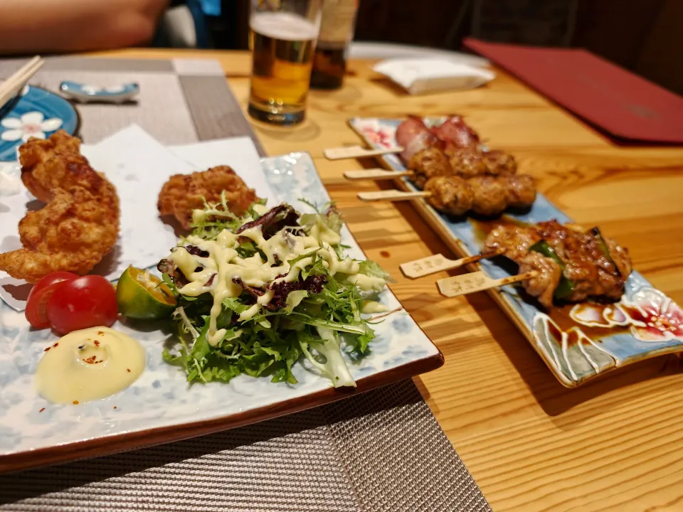 Fried shrimp, salad, skewers, and beer on a restaurant table.