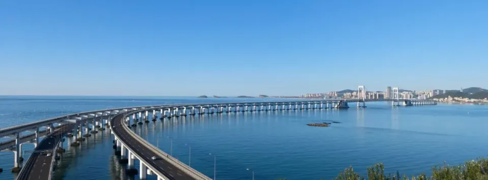 A sweeping view of Dalian's sea bridge curving across calm blue water.