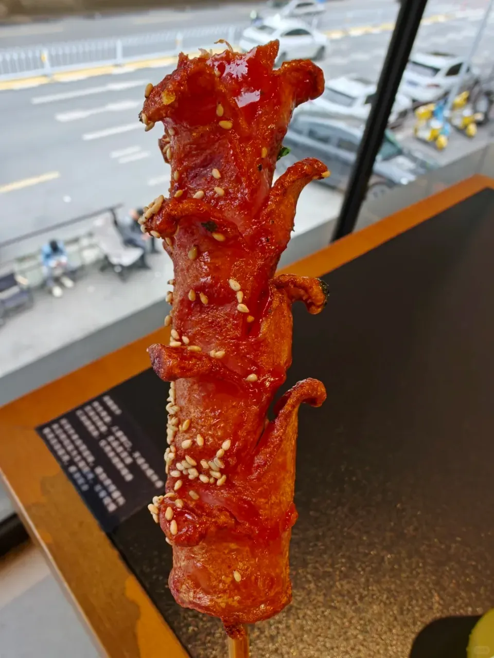 A close-up of a glazed grilled skewer held beside a window.