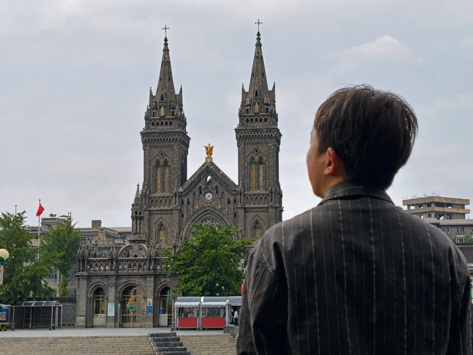 A person looking toward a church with twin pointed towers.