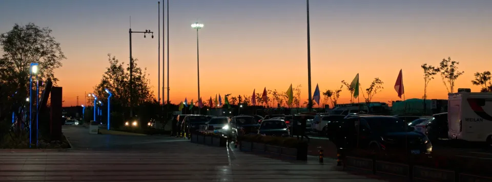 An orange evening sky above a parking area lined with flags.