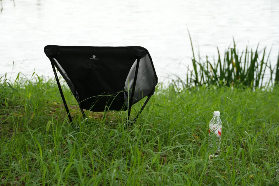 A black camping chair and a bottle of water beside the lake.
