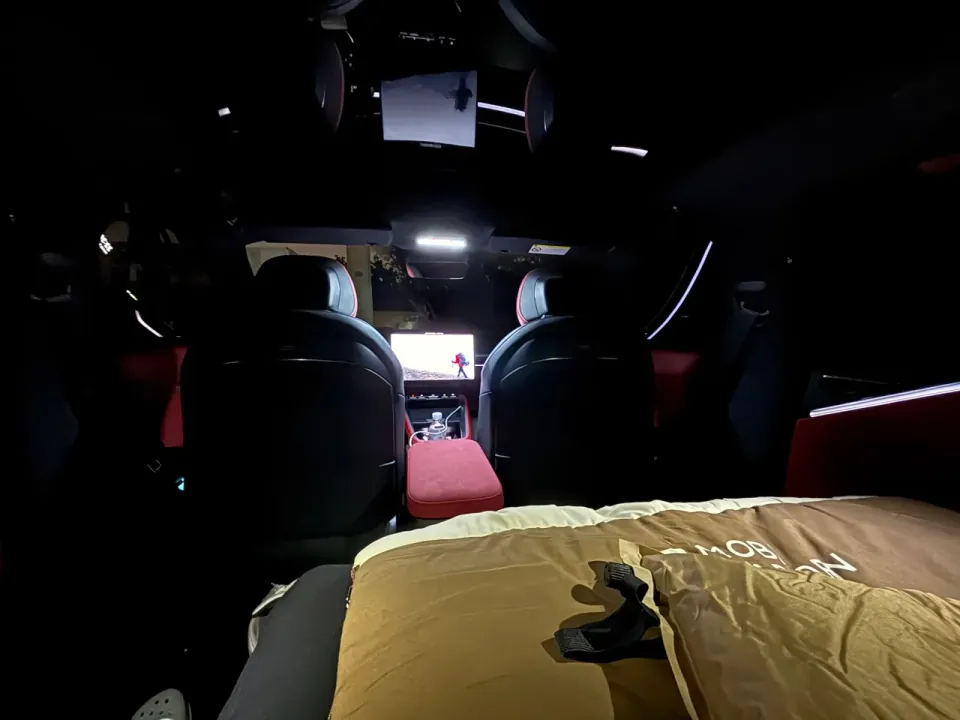 A dark car interior viewed from the sleeping area toward the front seats.