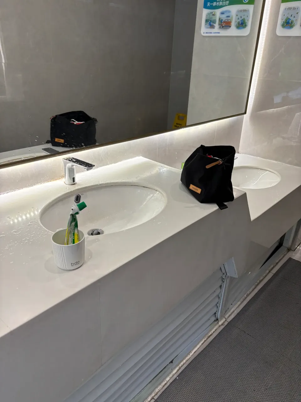 A clean restroom counter with two sinks, a toothbrush, and a toiletry bag.