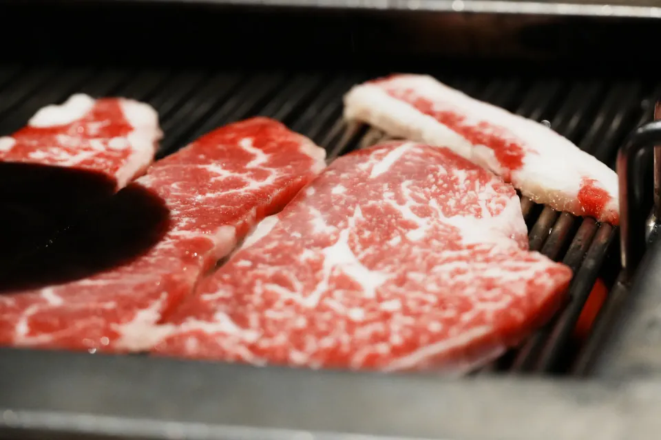 Raw marbled beef slices cooking on a grill.