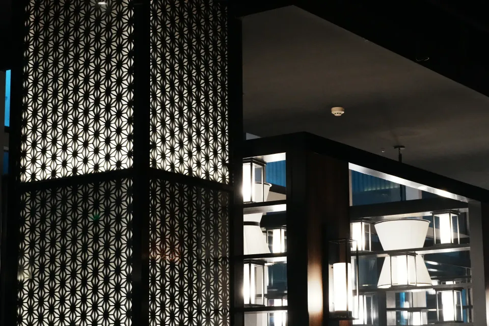 Dark geometric screens and illuminated lantern shelves inside a restaurant.