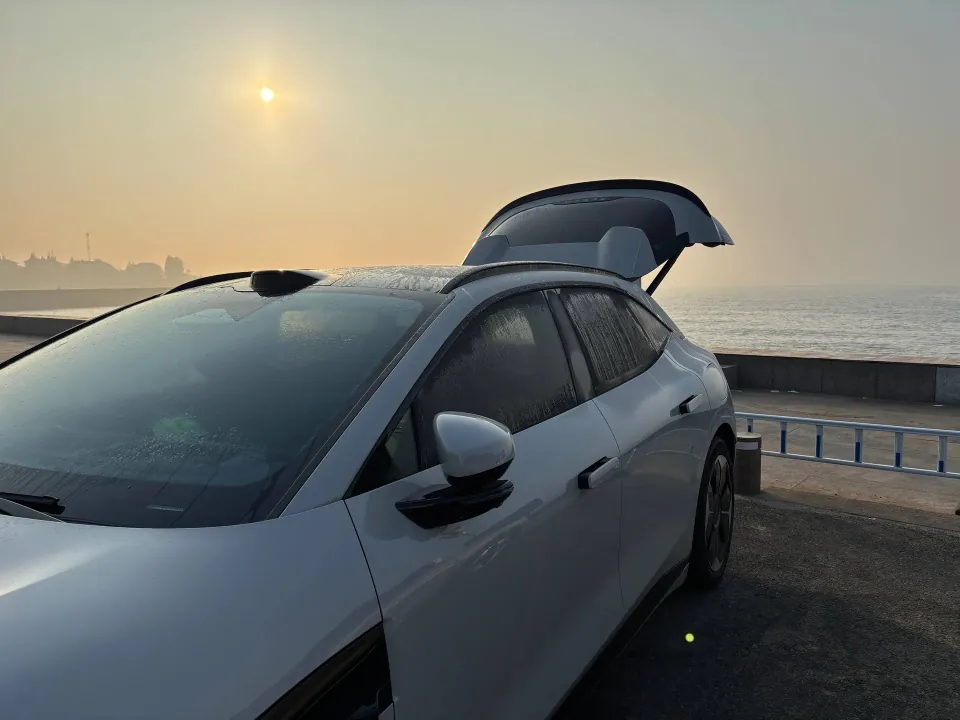 White Zeekr parked by the sea with its hatch open at sunrise