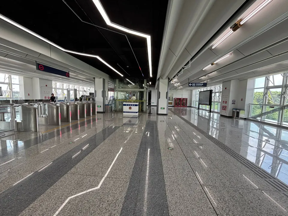 A bright metro station concourse with ticket gates and angular ceiling lights.