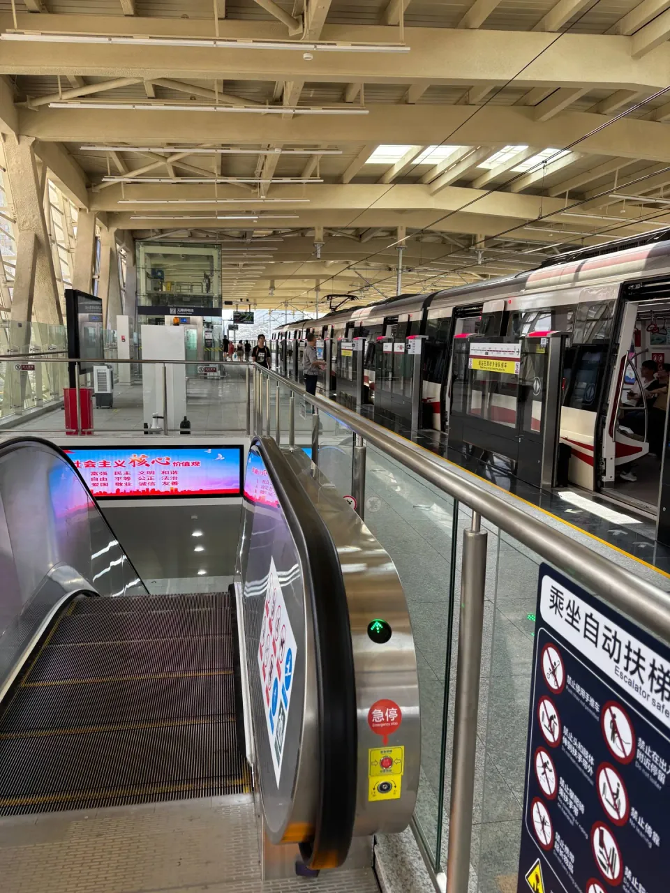 An escalator descends from an elevated metro platform beside a stopped train.