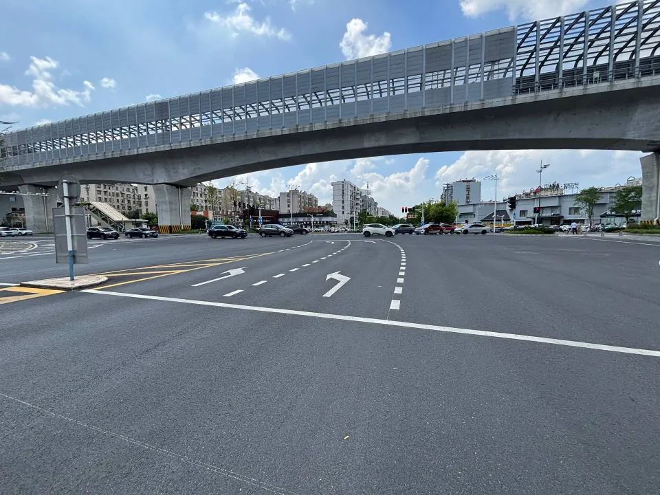 A wide intersection beneath an elevated metro viaduct.