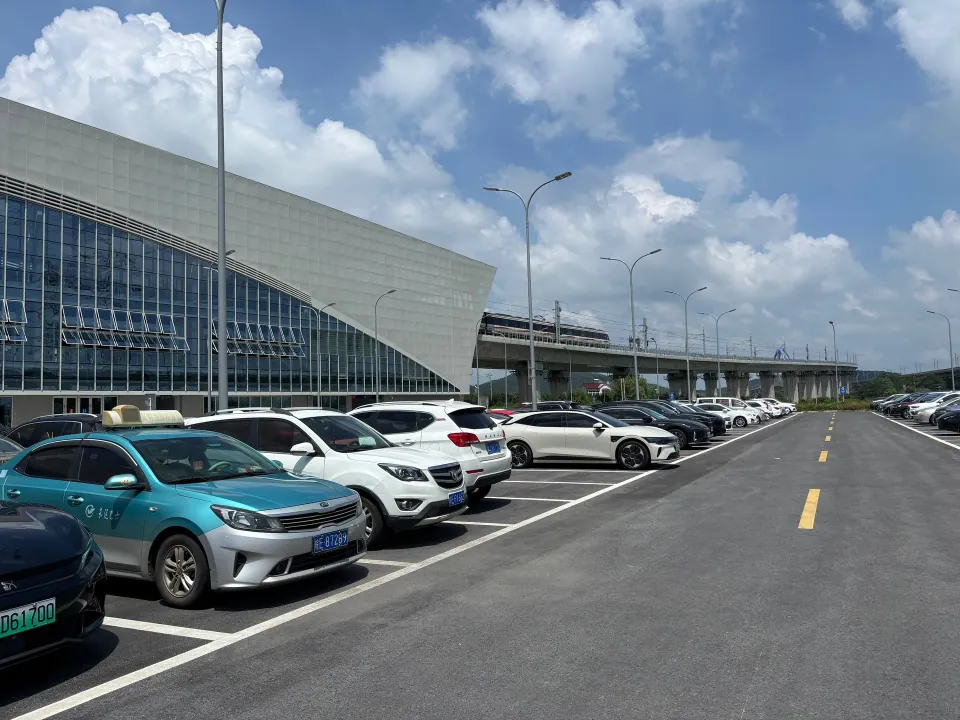 Cars parked outside a modern metro station beneath a blue sky.