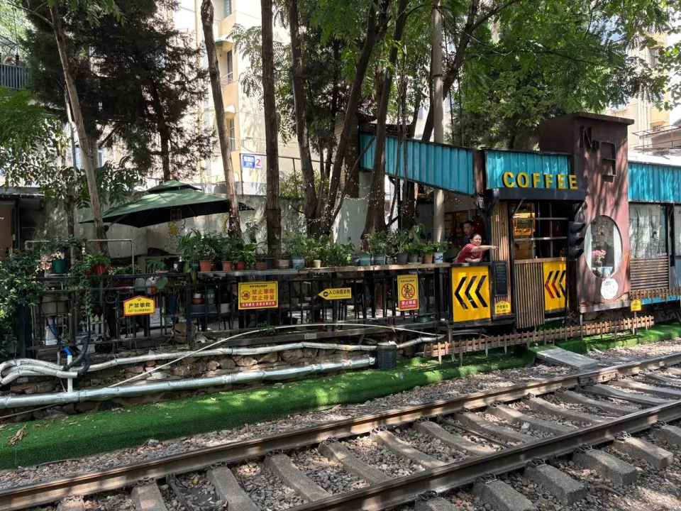 A small coffee shop beside railway tracks beneath leafy trees.