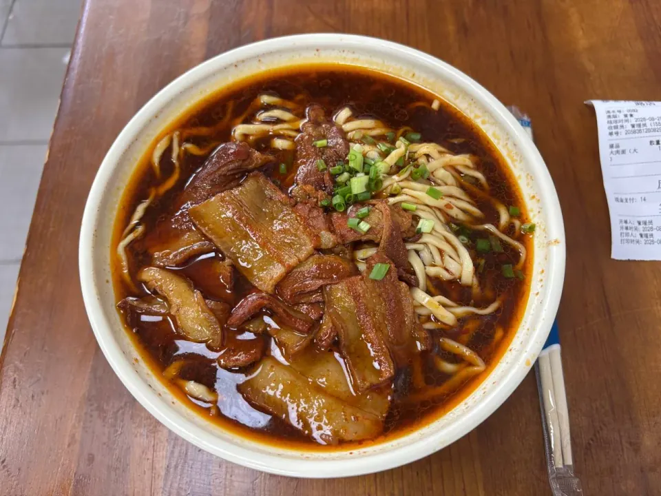 A bowl of noodle soup topped with thick slices of braised pork and scallions.