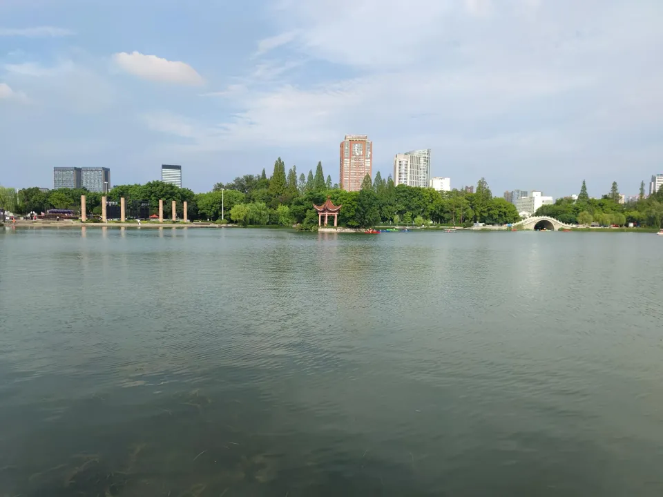 A lake with trees, a white arched bridge, and buildings on the opposite shore.