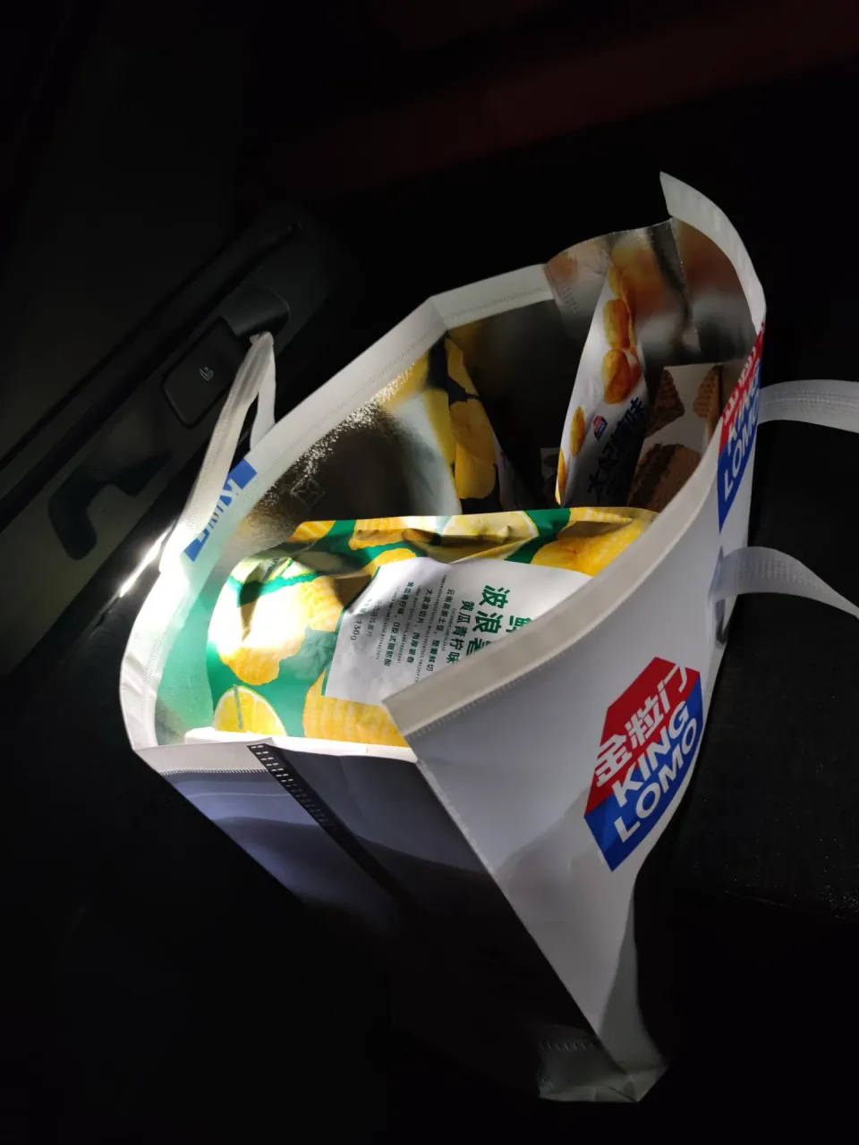 A shopping bag filled with packaged snacks rests inside a car.