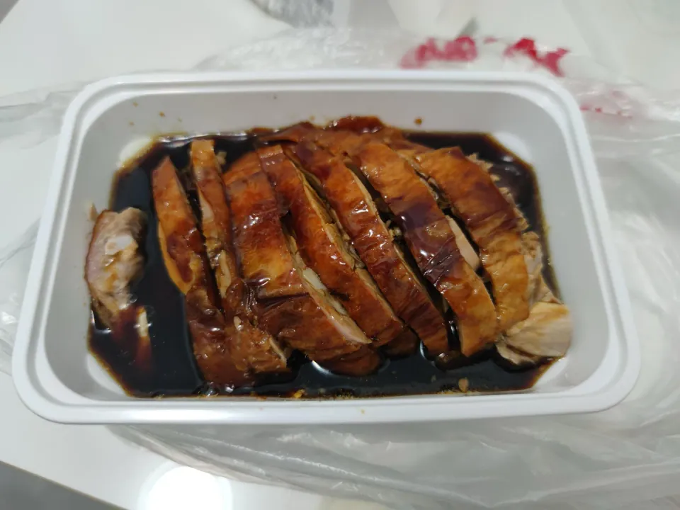 Sliced roast meat sits in dark sauce in a takeaway container.