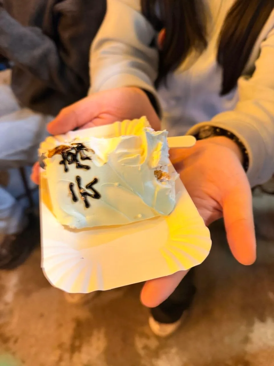 A person holds a small birthday cake with pale blue and yellow frosting.