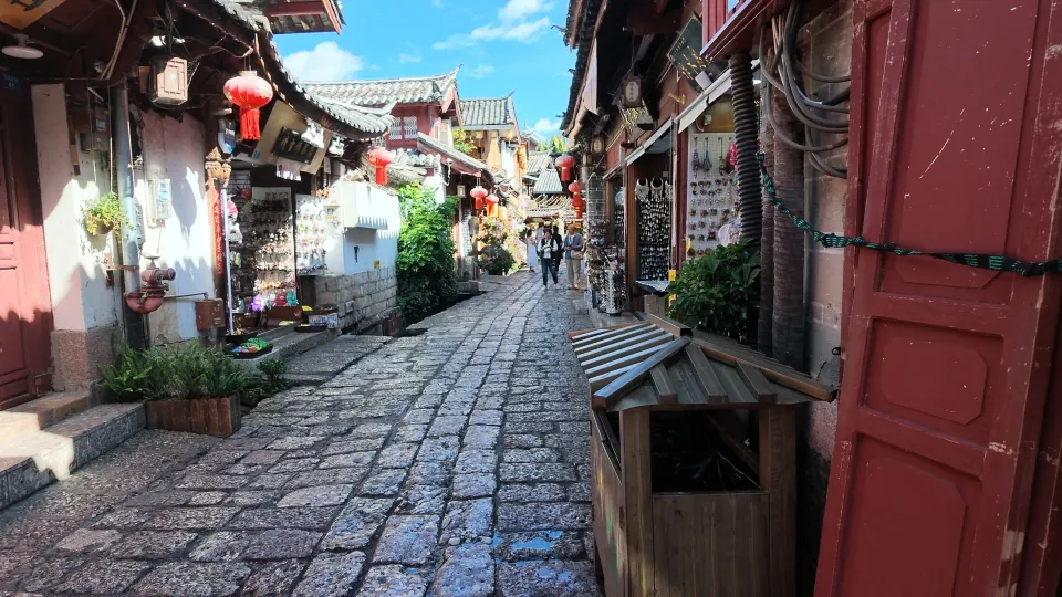 A cobbled lane passes traditional shops with wooden doors and red lanterns.