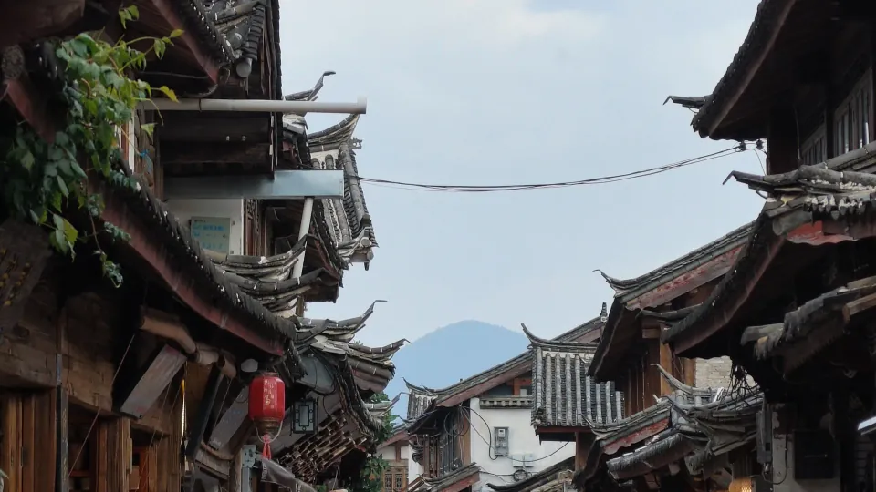 Traditional tiled rooftops frame a distant mountain beneath an overcast sky.