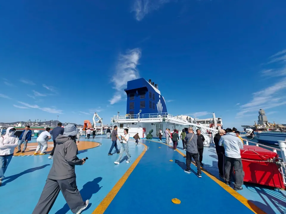 Passengers enjoying the sunshine on the ferry's blue open deck.