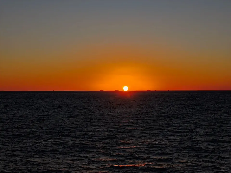 The setting sun touching the sea beneath a glowing orange sky.