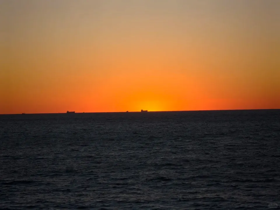 Ships silhouetted against the orange glow of sunset on the horizon.