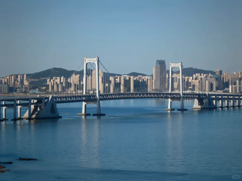 Suspension bridge towers framed by waterfront buildings and hills.