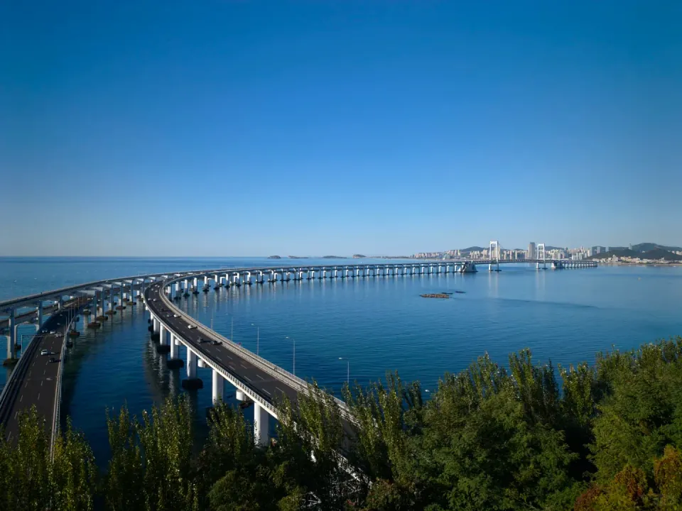 Dalian's sea bridge stretching across the bay beyond green trees.