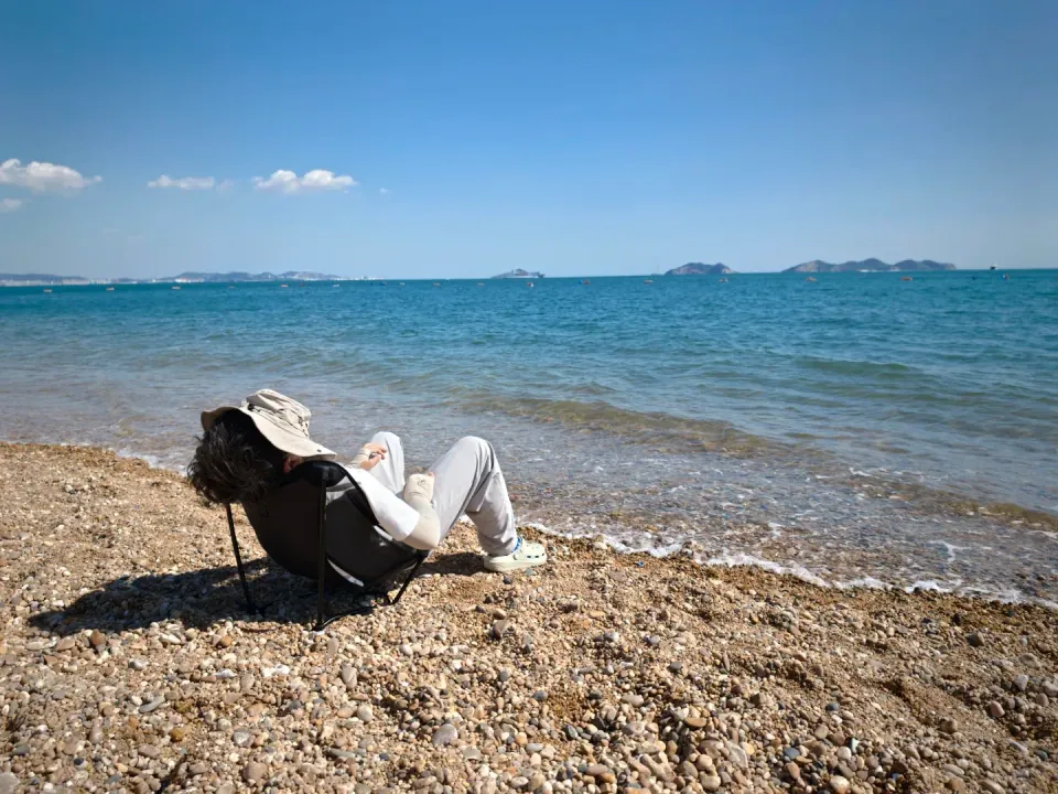 A person relaxing in a folding chair on the pebble beach.