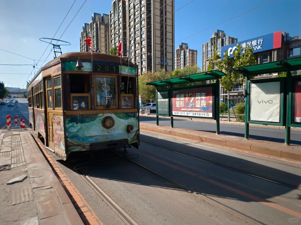 A vintage green tram approaching a street-side stop in Dalian.