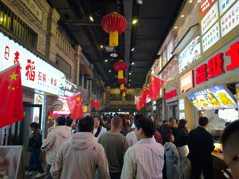 A crowded covered food street decorated with red lanterns and flags.